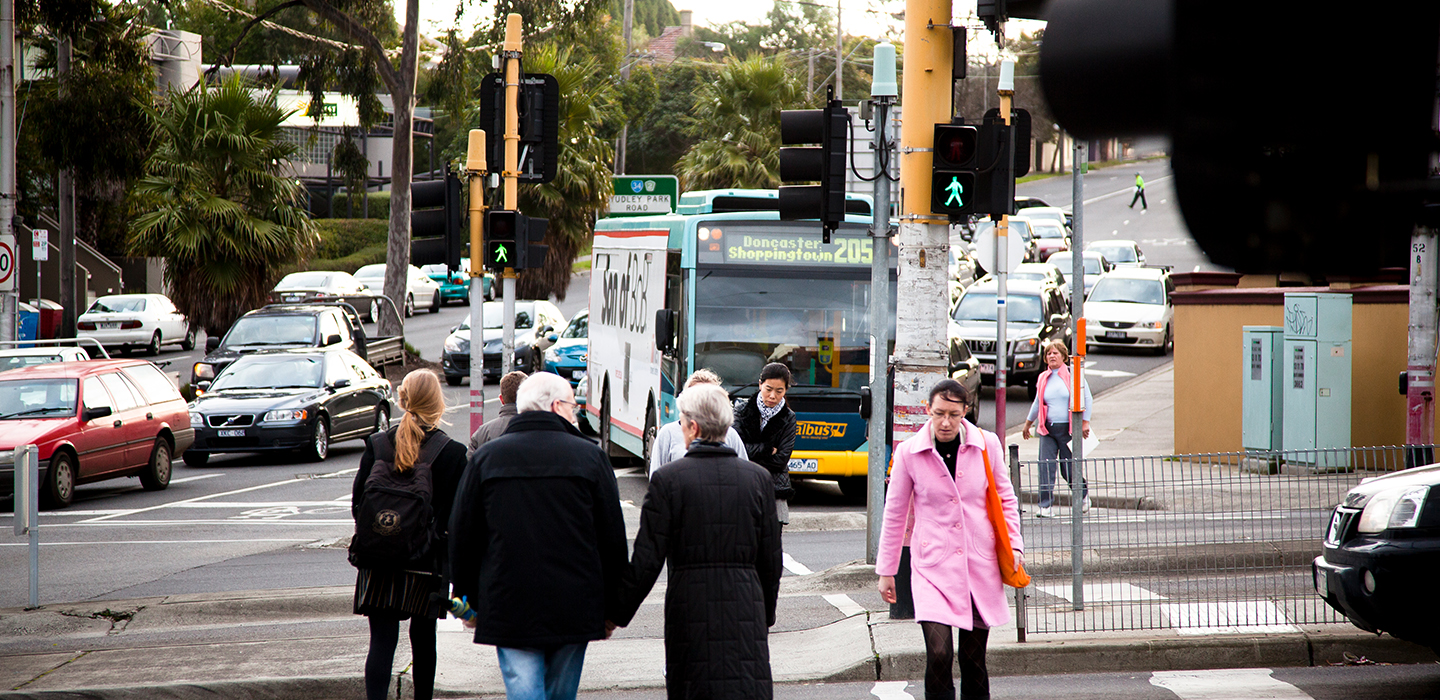People crossing a busy road of cars and buses